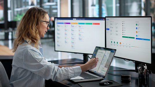 Woman at desk looking at multiple computer screens.