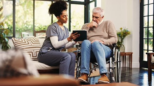 A healthcare worker sitting next to a man in a wheelchair, going over a form