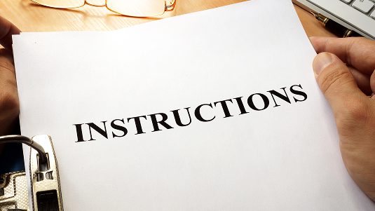 A paper on a desk near a pair of glasses, pen and keyboard; that says "Instructions" on it.