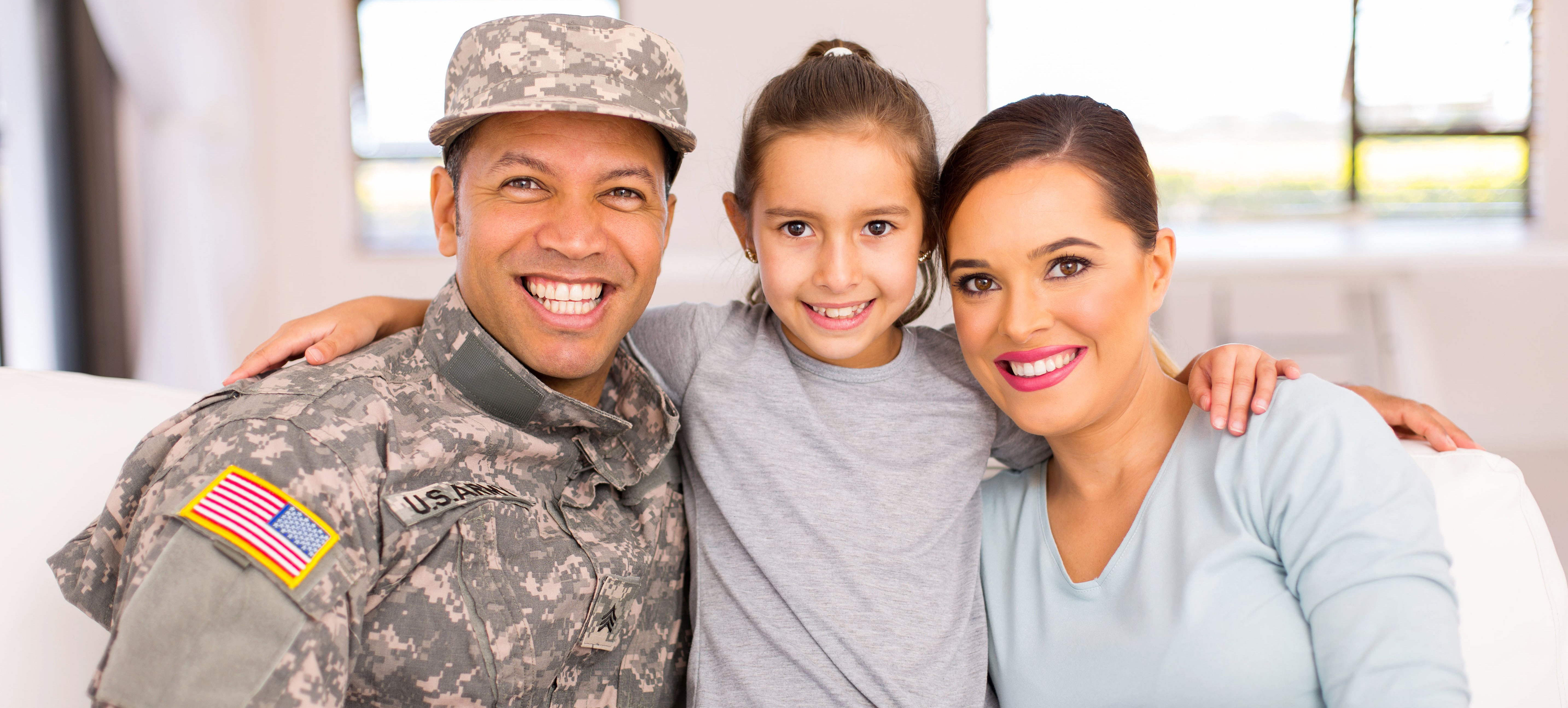 Man in US Army uniform hugging a woman and child